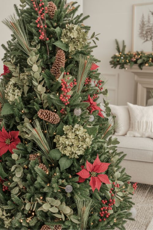 Christmas tree decorated with berry sprays, faux hydrangea stems, pinecone picks, and poinsettias to fill gaps and create a lush look
