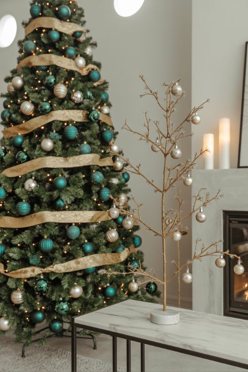 A festive living room featuring 2025 Christmas tree trends with a fully decorated showpiece tree, a tabletop tree, oversized bows, and a starburst topper for a dramatic and elegant holiday look