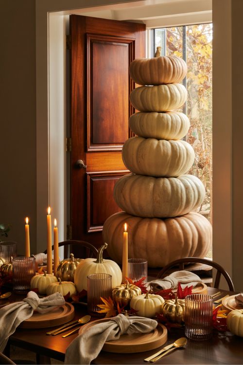 Fall Thanksgiving decor with oversized white pumpkins by the entryway and a dining table styled with gold mini pumpkins, candles, and autumn leaves for a cozy harvest atmosphere.