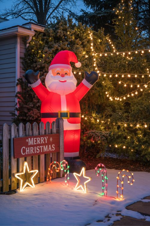 Front yard decorated for Christmas with twinkling LED lights, life-sized Santa and snowmen inflatables, rustic wooden decorations, and DIY wire-frame stars and candy canes.