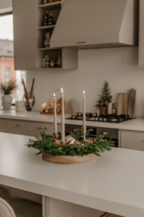 A kitchen island decorated for Christmas in a minimalist style with a wooden tray, a few candles, and a small evergreen arrangement, creating an elegant and uncluttered holiday centerpiece