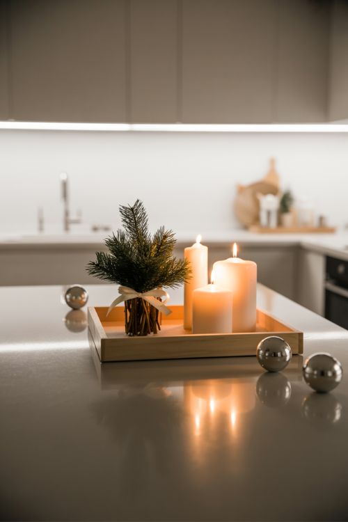 A kitchen island decorated for Christmas in a minimalist style with a wooden tray, a few candles, and a small evergreen arrangement, creating an elegant and uncluttered holiday centerpiece