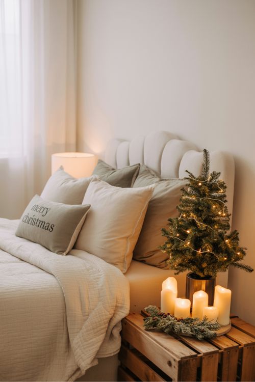 Neutral Christmas bedroom and cozy nook with white and cream bedding, muted pillows, small tabletop trees, candles, and greenery-filled vintage crates, creating a peaceful, cozy, and festive holiday atmosphere.