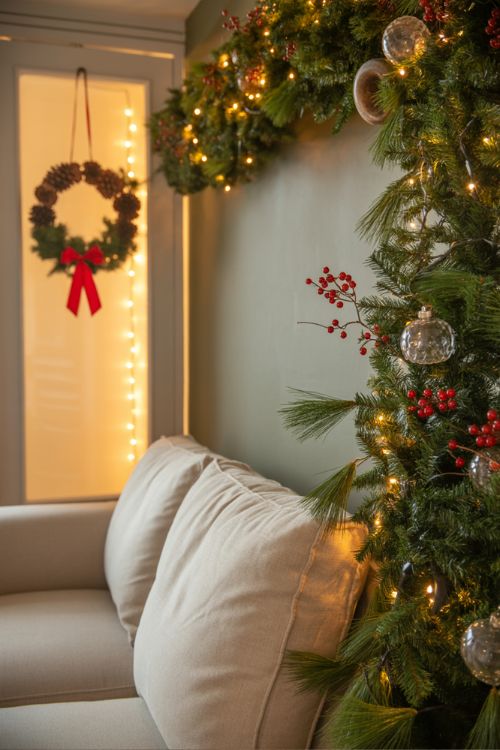 Small apartment interior decorated with Christmas garlands on shelves and mantel, and a festive wreath on the door, showcasing cozy, space-saving holiday decor ideas