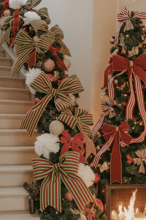 A festive Christmas living room featuring striped and statement bows on the tree, staircase, and dining chairs with oversized velvet and ribbon details for a playful, nostalgic holiday look