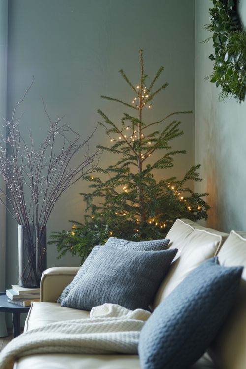 Minimal winter living room with greenery, muted grays, soft blues, and a small tree with twinkle lights for a cozy post-Christmas transition