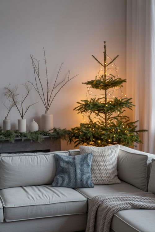 Minimal winter living room with greenery, muted grays, soft blues, and a small tree with twinkle lights for a cozy post-Christmas transition