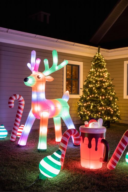 Christmas yard featuring smart color-changing lights, moving inflatables, oversized candy canes, giant hot chocolate cups, snow globes, and pre-lit trees, blending tech-savvy and DIY trends.