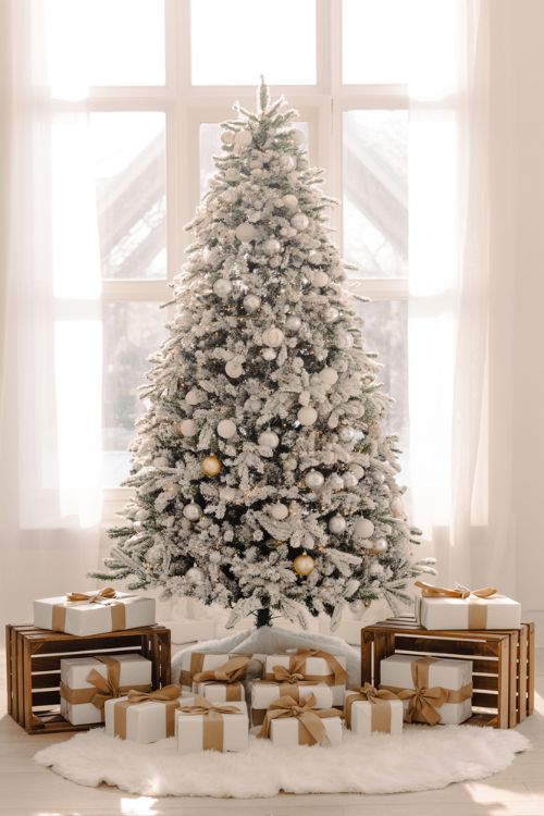 White Christmas tree decorated with silver, gold, and pastel ornaments, soft fairy lights, and a white faux fur tree skirt in a cozy modern living room