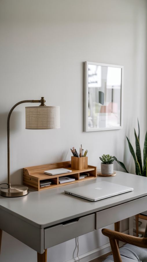 Create a realistic minimalist small home office that emphasizes decluttering and clean design. Include a simple desk with only essential items like a laptop, sleek desk organizer, and a stylish lamp. Show digitized document storage or hidden drawers to reduce visible clutter. Use neutral tones such as white, beige, or light gray, with natural light streaming in to enhance openness. Add subtle decorative elements like a small plant or minimal wall art. The overall feel should be calm, airy, and organized, highlighting how minimalism maximizes space and promotes focus in a compact workspace.