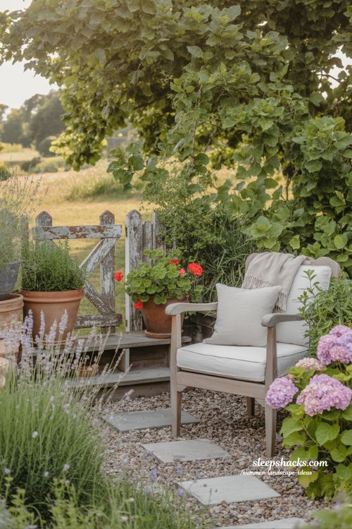 small backyard gravel patio with plants in pots and wooden chair and summer flowers