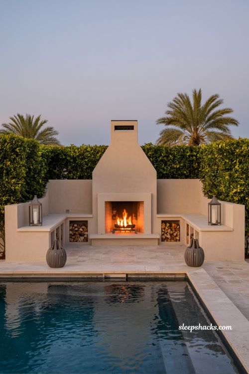 Backyard pool with statement outdoor stucco fireplace and built-in seating luxury Mediterranean style garden design with warm evening lighting