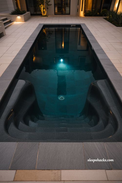 Dark shell fiberglass pool with dramatic nighttime lighting and modern luxury backyard design with high contrast minimalist outdoor aesthetic