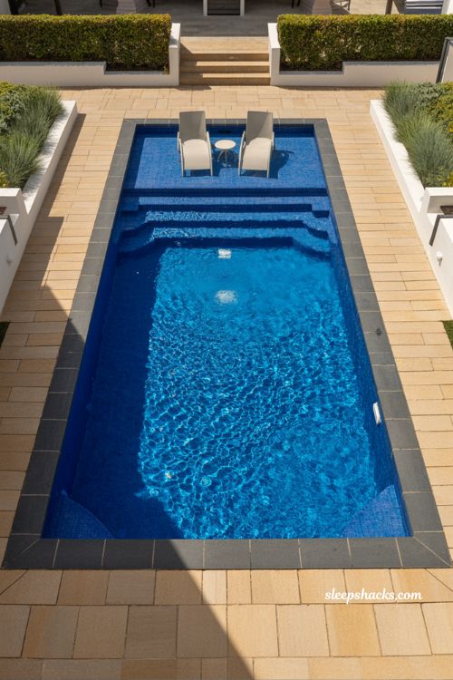 Classic rectangle fiberglass pool with tanning ledge and minimalist modern backyard design in deep blue water and charcoal stone deck