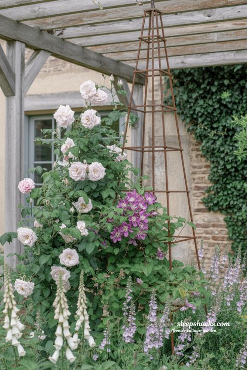 French cottage garden vertical interest ideas featuring climbing roses and clematis on vintage wooden arches and iron trellises