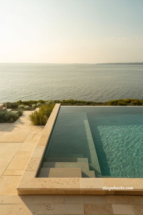Infinity pool on waterfront with travertine paving and horizon aligned edge blending into ocean view luxury coastal landscape design
