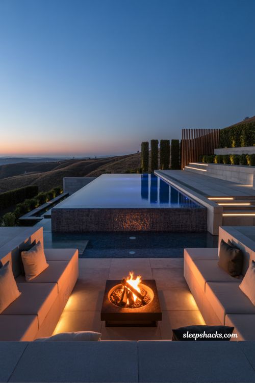 Infinity pool with fire pit lounge zone at sunset in luxury modern hillside backyard with infinity edge and dramatic evening lighting