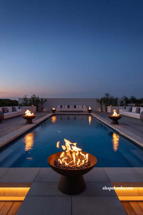 Poolscape with fire bowls at night modern luxury backyard pool with reflective water and warm lighting and dramatic twilight atmosphere