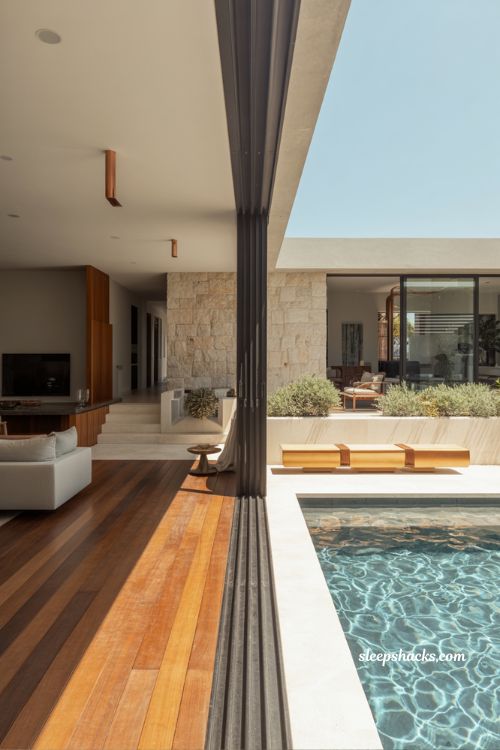Seamless indoor outdoor living pool design with timber decking limestone walls and modern architectural garden integration