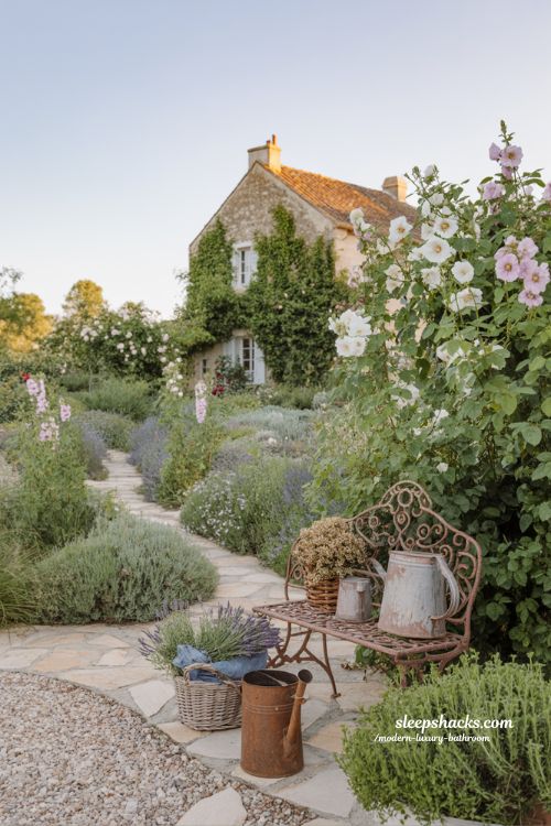 Winding stone pathway through an authentic French cottage garden with overflowing flowers and herbs in front of an old farmhouse