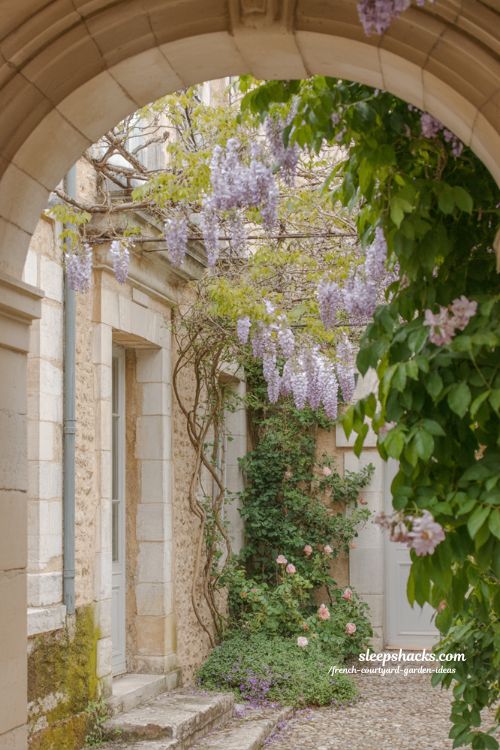 french courtyard garden with climbing wisteria roses and stone archway softened by natural flowing greenery