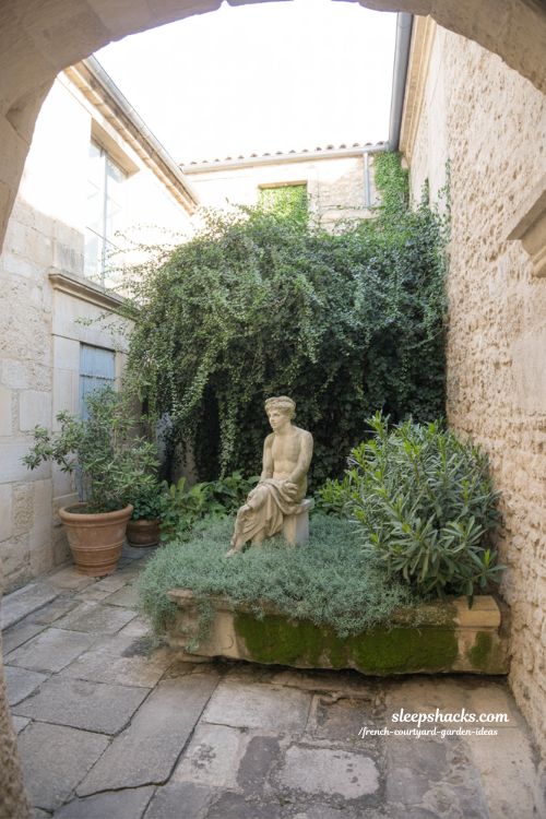 french courtyard garden with small sculpture hidden among plants creating quiet focal point and discovery feeling