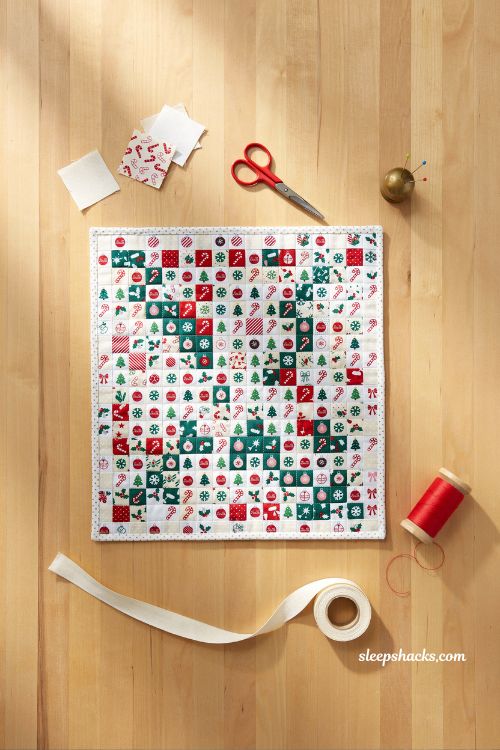 Baubles mini quilt with 2.5 inch charm squares Christmas ornament patchwork wall hanging on wooden craft table with festive holiday sewing aesthetic