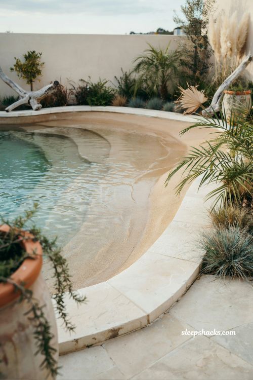 Beach entry pool with sand-toned plaster finish creating a natural shoreline aesthetic and coastal backyard design