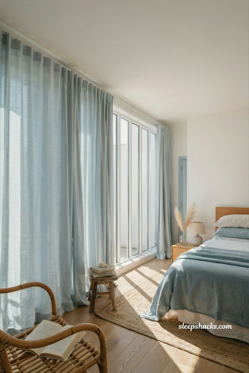 Coastal blue bedroom ideas with pale blue linen curtains and airy light filled beach house style