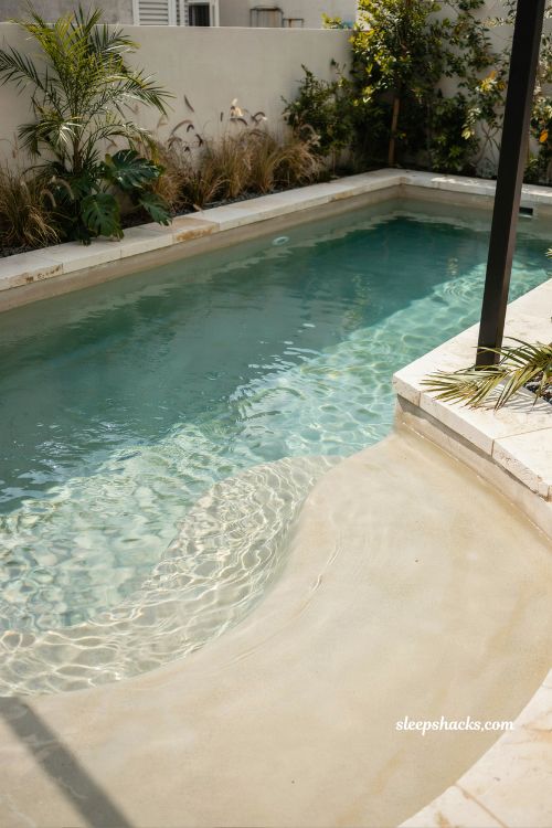 Compact beach entry pool in small backyard corner with space-saving plunge pool design and coastal minimal style