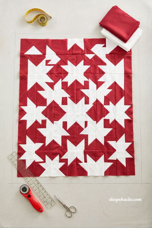 Knitted star two tone christmas quilt bold red and white geometric star patchwork quilt laid flat in minimalist modern sewing studio with Scandinavian holiday aesthetic