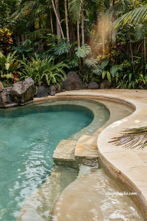Lagoon style beach entry pool with natural rock borders and tropical backyard retreat design