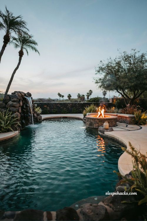 Lagoon style pool with rock waterfall and fire pit tropical backyard resort design with natural stone and warm ambient lighting