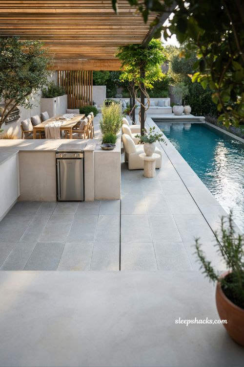 Luxury backyard pool with outdoor kitchen and dining pergola creating seamless modern entertainment space with poolside living and open-air cooking area
