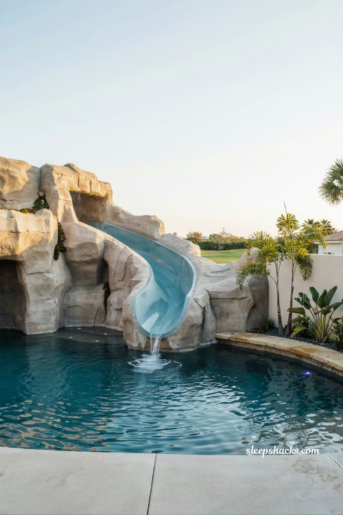 Modern backyard pool with built-in water slide and rock-inspired design creating a luxury family outdoor entertainment space