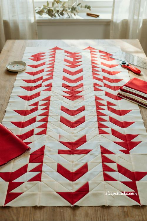Nordic delight flying geese christmas quilt top in red and white geometric chevron pattern on minimalist Scandinavian sewing table with clean holiday aesthetic