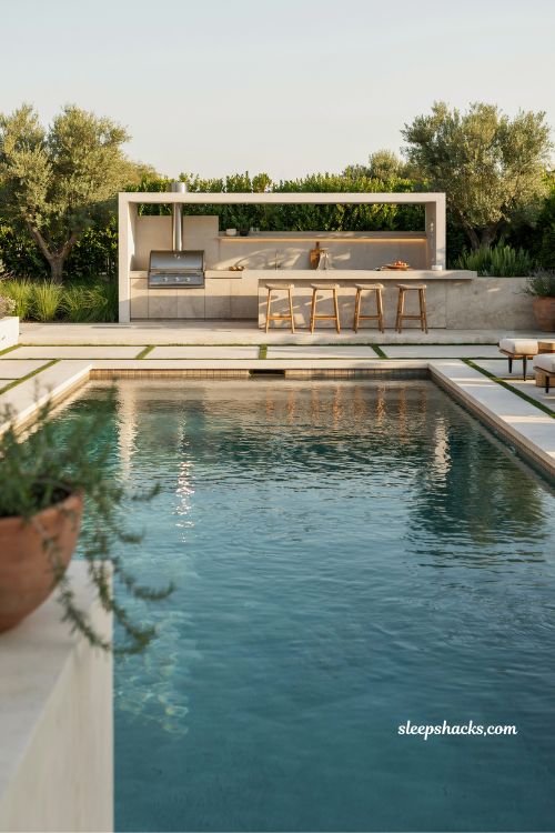 Outdoor kitchen and bar behind pool for functional backyard entertaining design