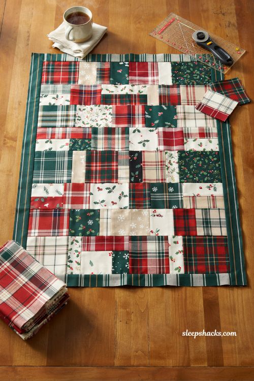 Patchwork plaid christmas quilt layout using squares and rectangles in red green and cream flannel style pattern on cozy farmhouse sewing studio table with curated holiday fabric collection