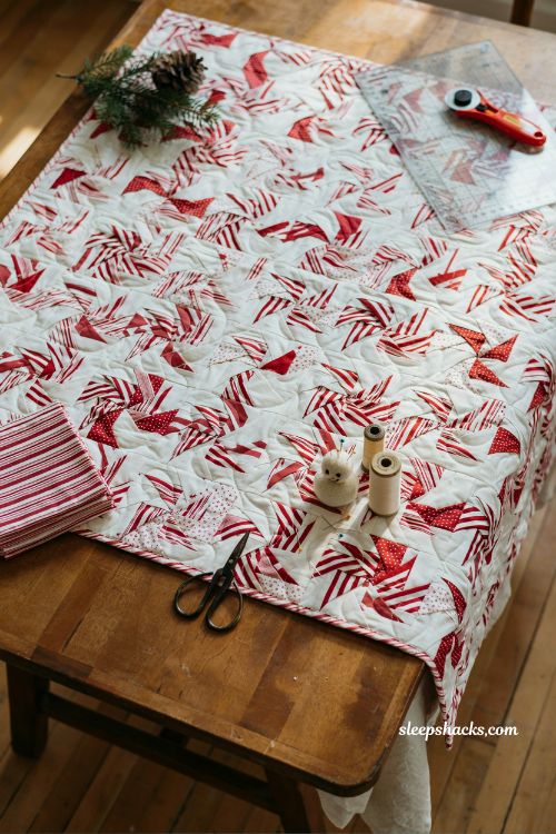 Peppermint pinwheels christmas quilt with candy cane striped pinwheel blocks on vintage sewing table in cozy holiday quilting studio with retro festive charm