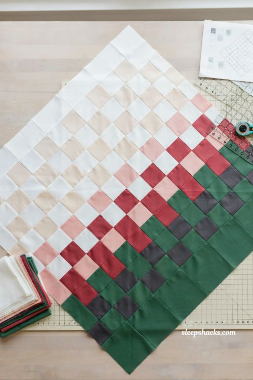Simple diamond patchwork christmas quilt laid in diagonal around the world layout using festive fat quarters on cozy sewing studio cutting table with gradient holiday fabric arrangement