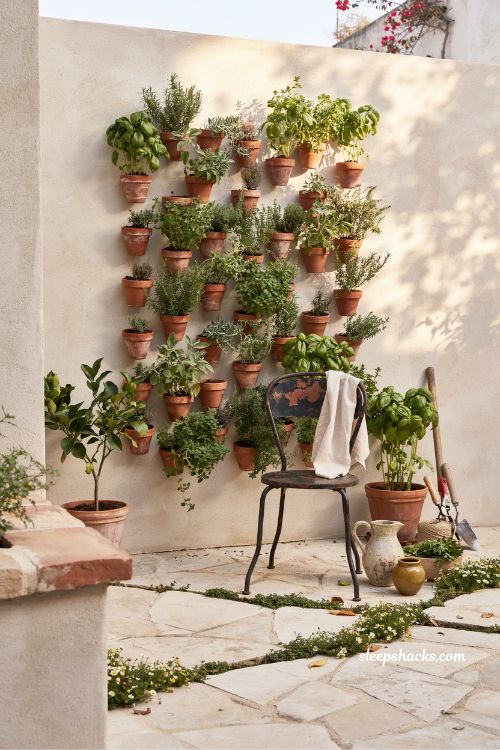 Small mediterranean garden ideas with a vertical herb wall filled with basil oregano and thyme in terracotta pots for small space gardening 