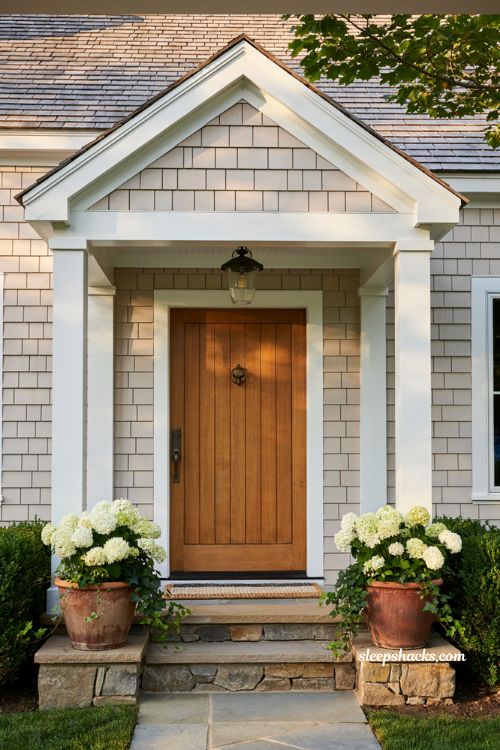 Farmhouse exterior portico entry ideas featuring a gabled covered front door with wooden columns and a hanging pendant light