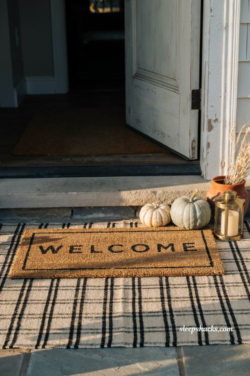 Layered outdoor rugs on front porch with plaid base mat and fall pumpkins for entry decor