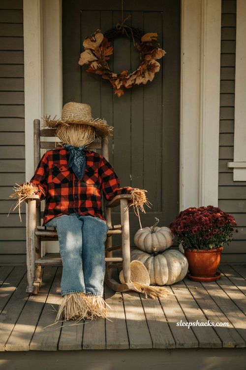 Old-fashioned scarecrow in a rocking chair on a front porch with autumn pumpkins and mums