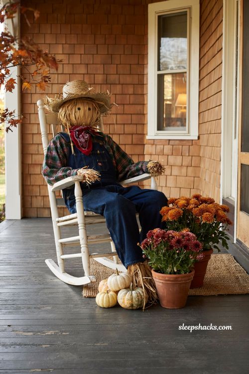 Rustic DIY outdoor fall scarecrow in a rocking chair on a cozy porch with mums and pumpkins