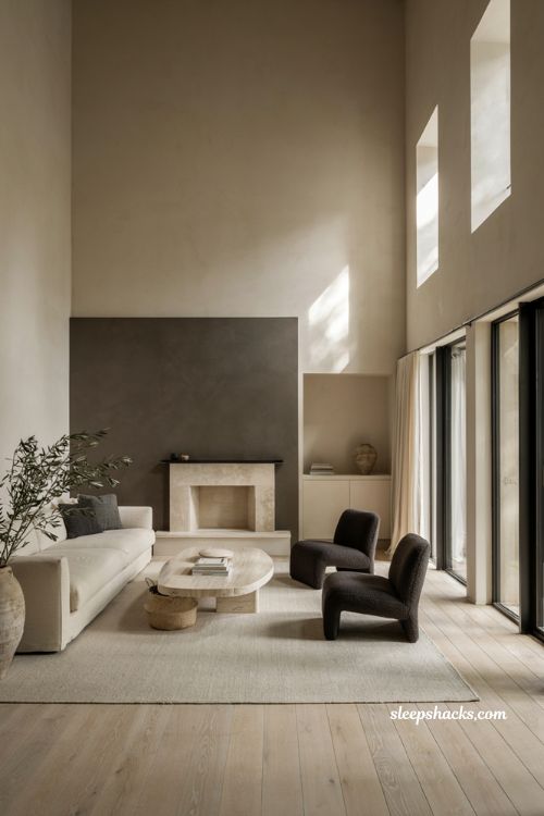 Wide-angle eye-level editorial interior photography of a sophisticated modern living room where a refined monochromatic palette creates a peaceful atmosphere, allowing architecture, natural light, and rich textures to become the focal point instead of bold color. Timeless contemporary architecture with minimalist and Scandinavian influences, featuring soaring ceilings, smooth warm-white plaster walls, a dramatic matte charcoal accent wall, floor-to-ceiling black steel-framed windows, wide-plank white oak flooring, custom built-in cabinetry with concealed storage, a minimalist limestone fireplace, and clean architectural lines that emphasize simplicity and proportion. The color palette is intentionally restrained with warm ivory, soft white, light greige, gentle gray, weathered limestone, matte charcoal, natural oak, and subtle black accents, creating a calm, grounding, and sophisticated interior. Carefully curated furnishings include a low-profile ivory linen sectional, a sculptural travertine coffee table, charcoal boucle lounge chairs, a textured wool area rug, handcrafted ceramic vases, stacked design books, linen curtains, woven baskets, and a few mature olive branches that introduce understated organic softness without disrupting the neutral composition. Soft morning sunlight pours through expansive windows, washing every wall, floor, fabric, and stone surface in warm natural light while highlighting the subtle variations in plaster, wood grain, linen weave, and limestone with crisp editorial clarity. The atmosphere feels serene, timeless, and quietly luxurious, demonstrating how a restrained monochromatic palette allows honest materials and thoughtful architecture to create lasting beauty, where soft neutral tones instantly calm the mind, layered natural textures add warmth and depth, and a few carefully placed black architectural accents provide elegant visual contrast without overwhelming the space. no people, no text, no watermarks, no blur, no bokeh, all surfaces in sharp focus, photorealistic, ultra-realistic, 4K resolution, editorial interior photography, Pinterest-worthy