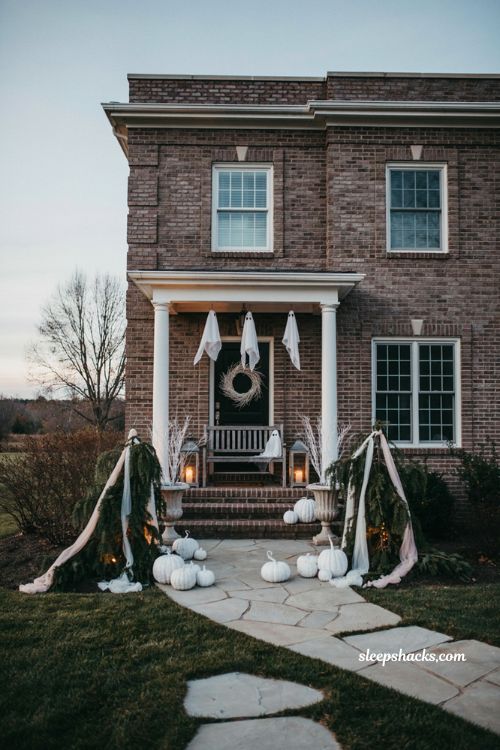 All white Halloween exterior decorations with cloth ghosts, white pumpkins, and pale fabric 