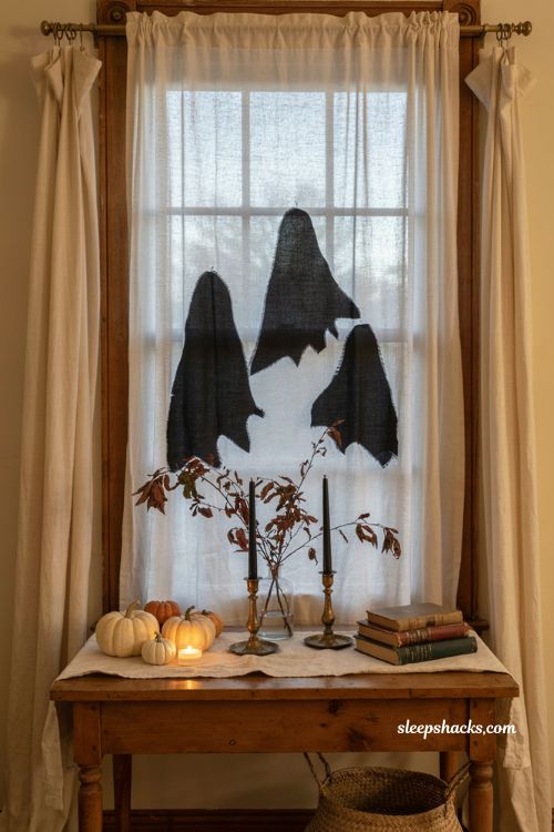 Black poster board ghost cutouts behind sheer curtains for Halloween windows