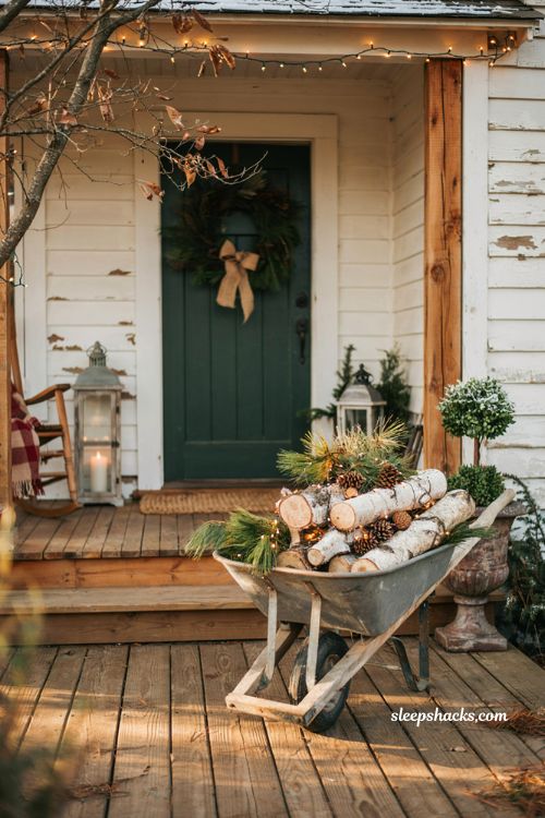 Country christmas porch with vintage wheelbarrow filled with birch logs and warm lights