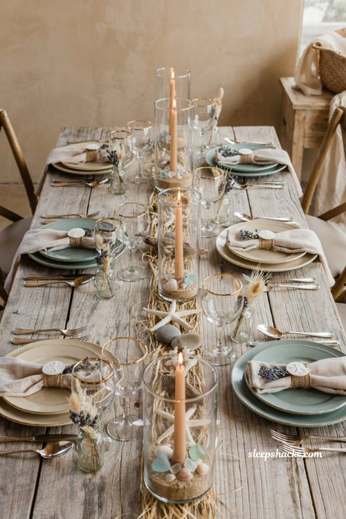 Cozy coastal baby shower centerpiece idea with sand and shell hurricane lanterns on a driftwood table